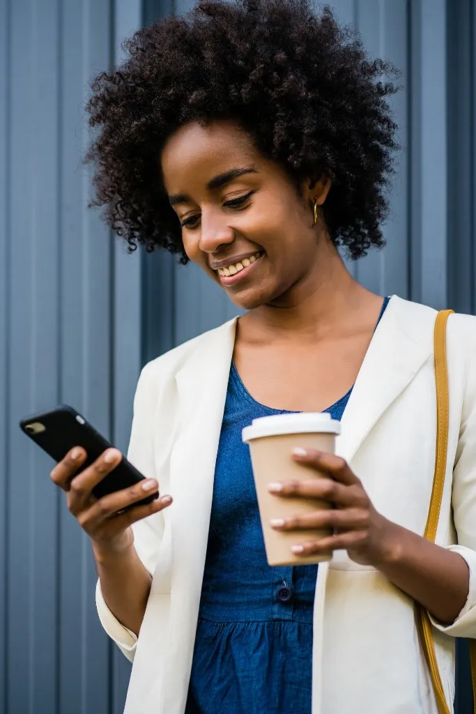 A woman with a coffee, smiling at a payment on her phone